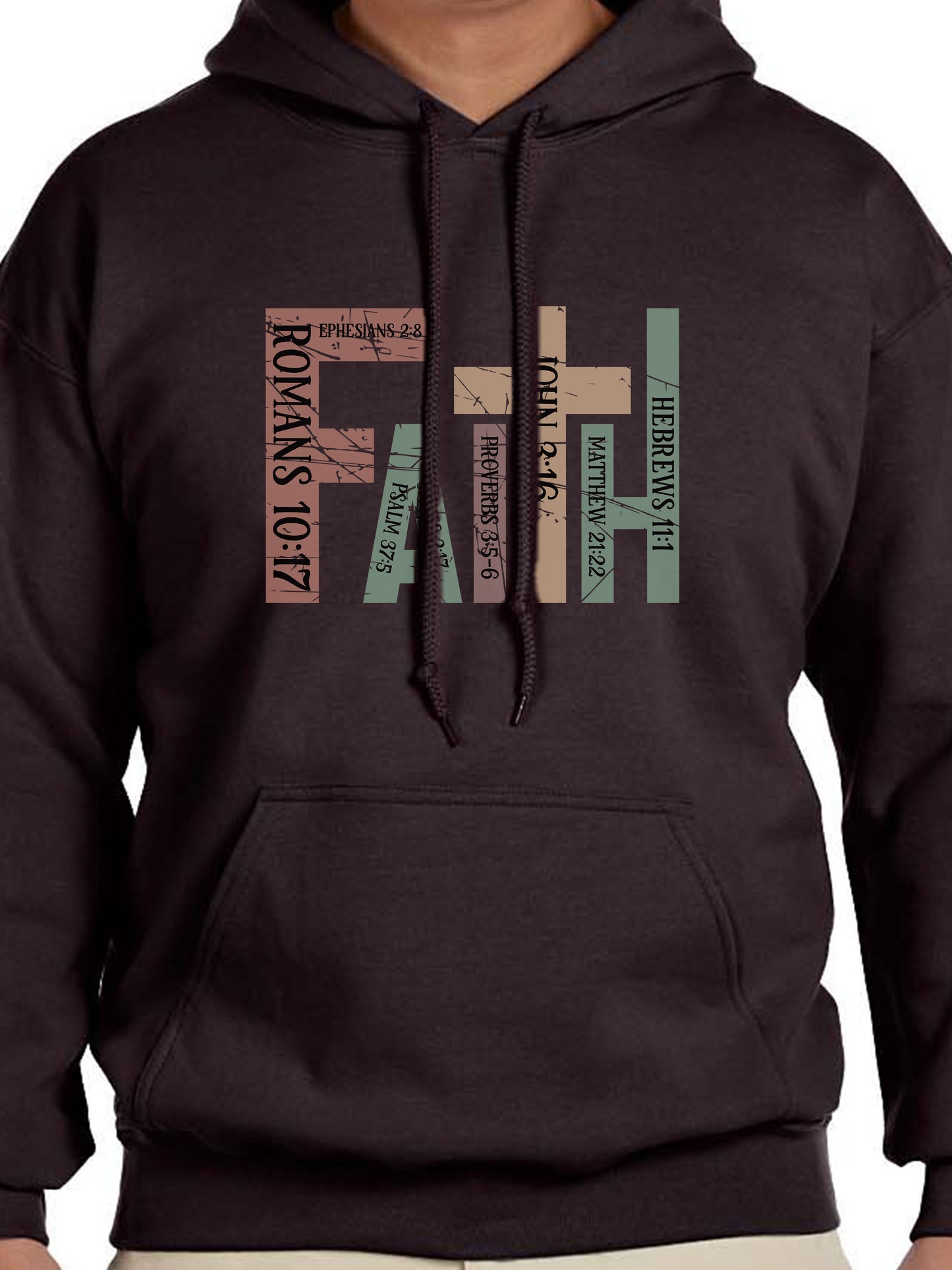 Man wearing a Dark Chocolate hoodie with the word “FAITH” printed in block letters across the chest. Each letter is filled with a Bible verse reference, including Romans 10:17, Ephesians 2:8, Psalm 37:5, Proverbs 3:5–6, John 3:16, Matthew 21:22, and Hebrews 11:1. The design combines bold typography and scripture for a powerful, faith-centered statement.