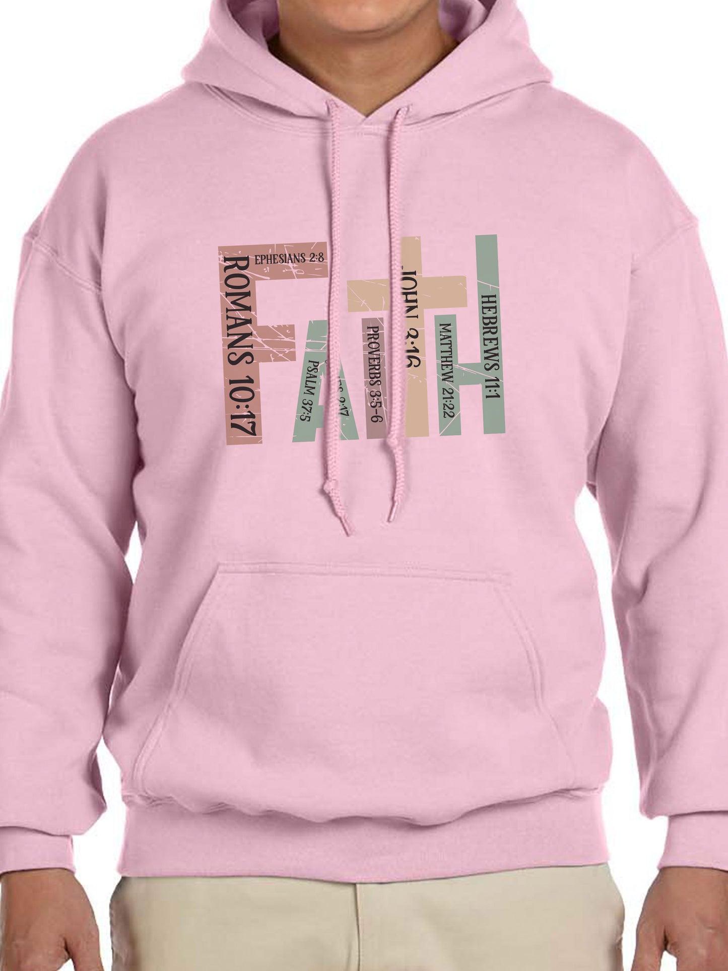 Man wearing a Light Pink hoodie with the word “FAITH” printed in block letters across the chest. Each letter is filled with a Bible verse reference, including Romans 10:17, Ephesians 2:8, Psalm 37:5, Proverbs 3:5–6, John 3:16, Matthew 21:22, and Hebrews 11:1. The design combines bold typography and scripture for a powerful, faith-centered statement.
