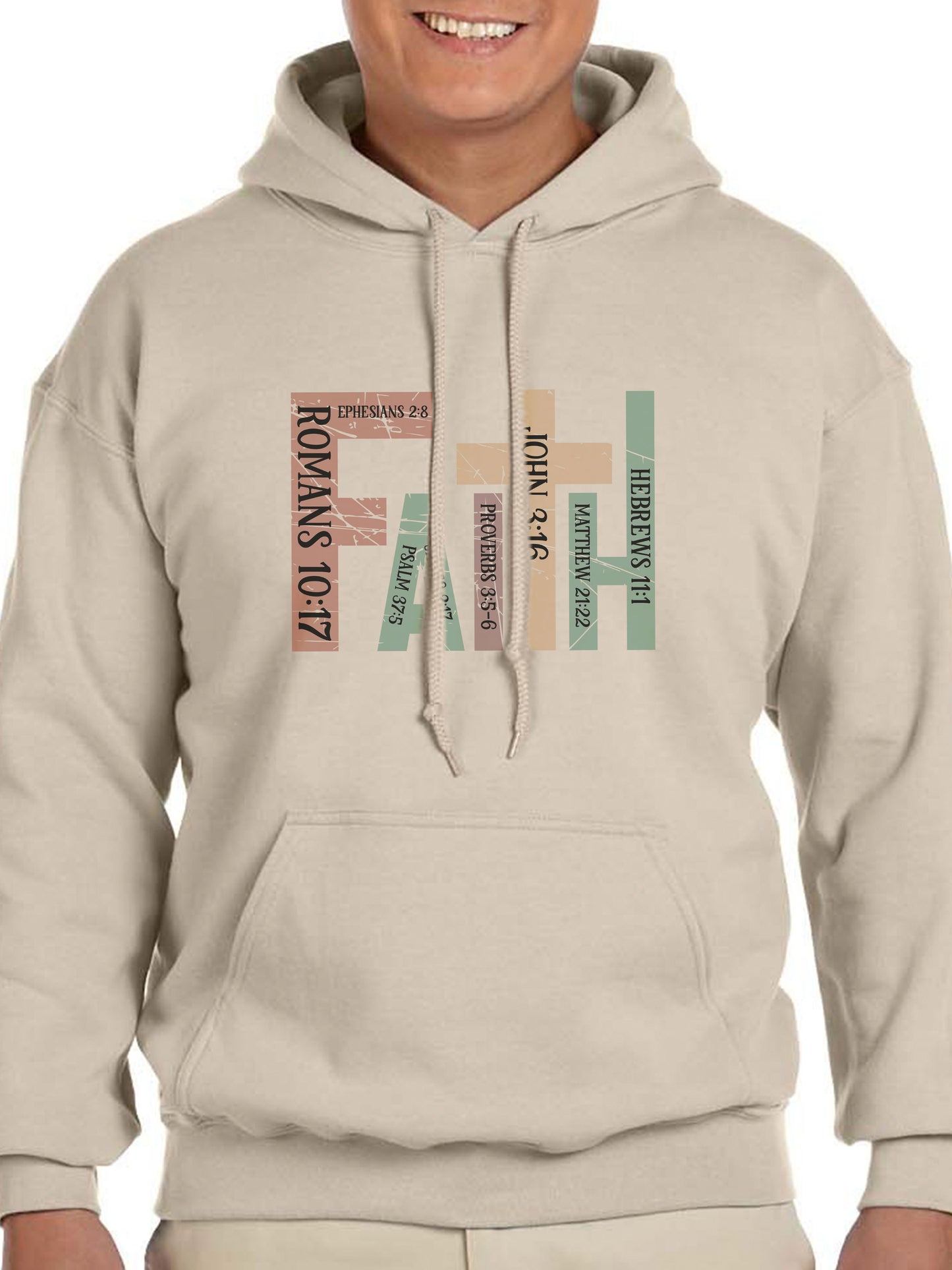 Man wearing a sand hoodie with the word “FAITH” printed in block letters across the chest. Each letter is filled with a Bible verse reference, including Romans 10:17, Ephesians 2:8, Psalm 37:5, Proverbs 3:5–6, John 3:16, Matthew 21:22, and Hebrews 11:1. The design combines bold typography and scripture for a powerful, faith-centered statement.