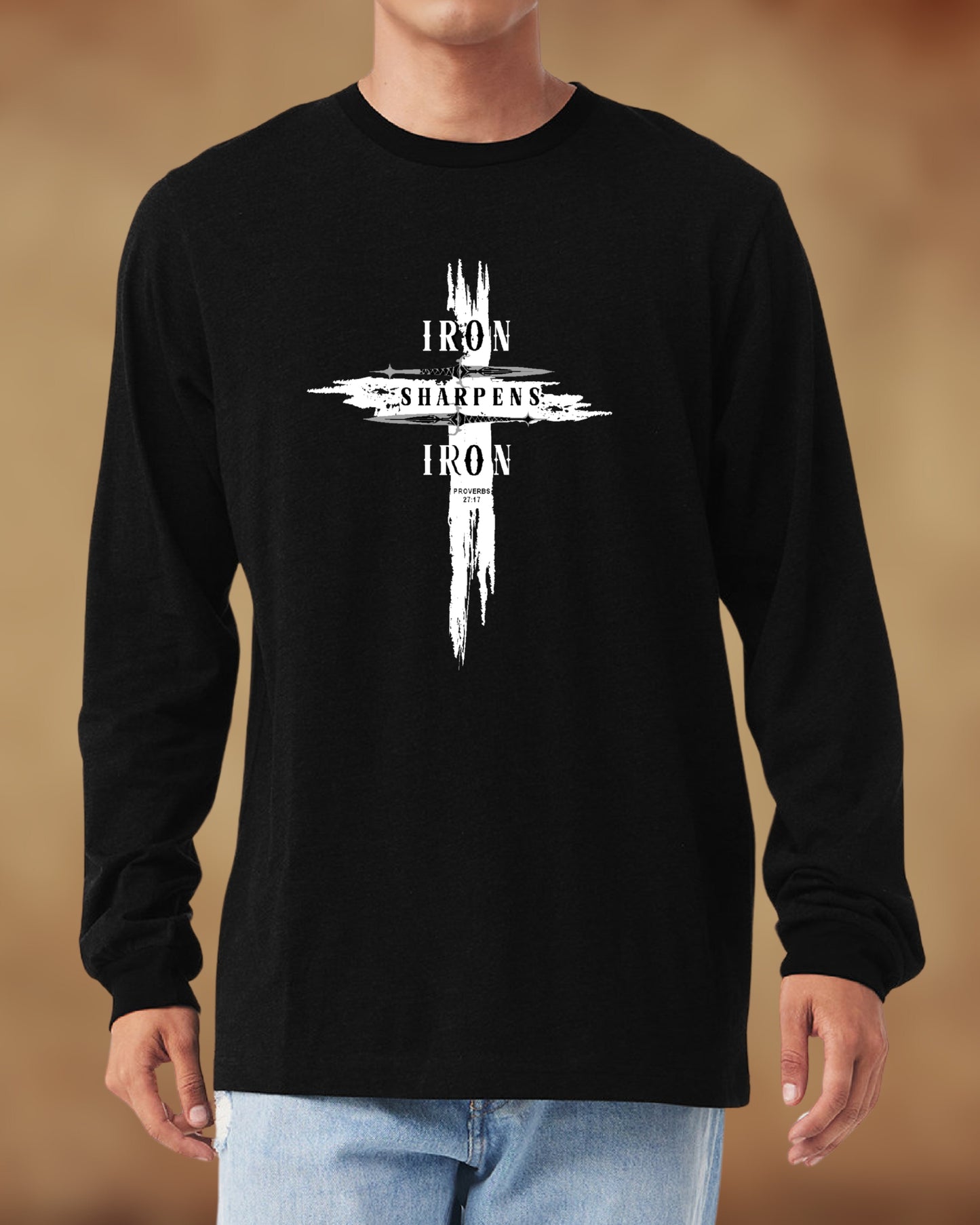 Man wearing a black long-sleeve shirt with a bold white cross design that reads “Iron Sharpens Iron – Proverbs 27:17.” The graphic features a distressed, brushstroke effect for a rugged and faith-driven look, perfect for Christian men who lead with strength and purpose.