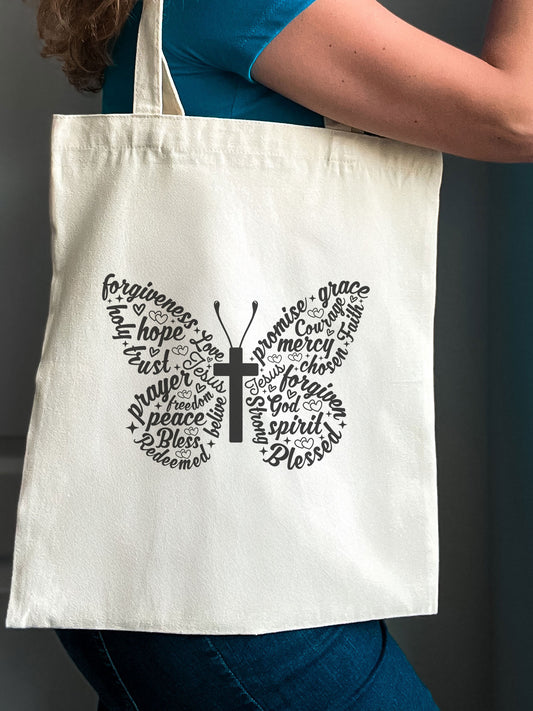 Woman carrying a Christian tote bag with a butterfly design made of inspirational words and a cross in the center.