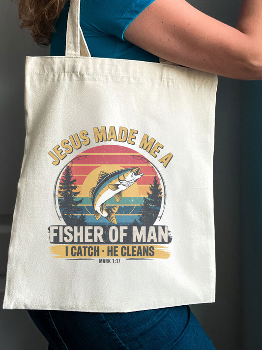 Woman holding a Christian tote bag that says “Jesus made me a fisher of man – I catch, He cleans” with a colorful fish design.