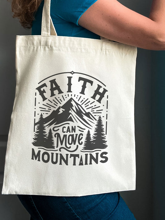 Natural canvas tote bag with black mountain design and the phrase “Faith Can Move Mountains”