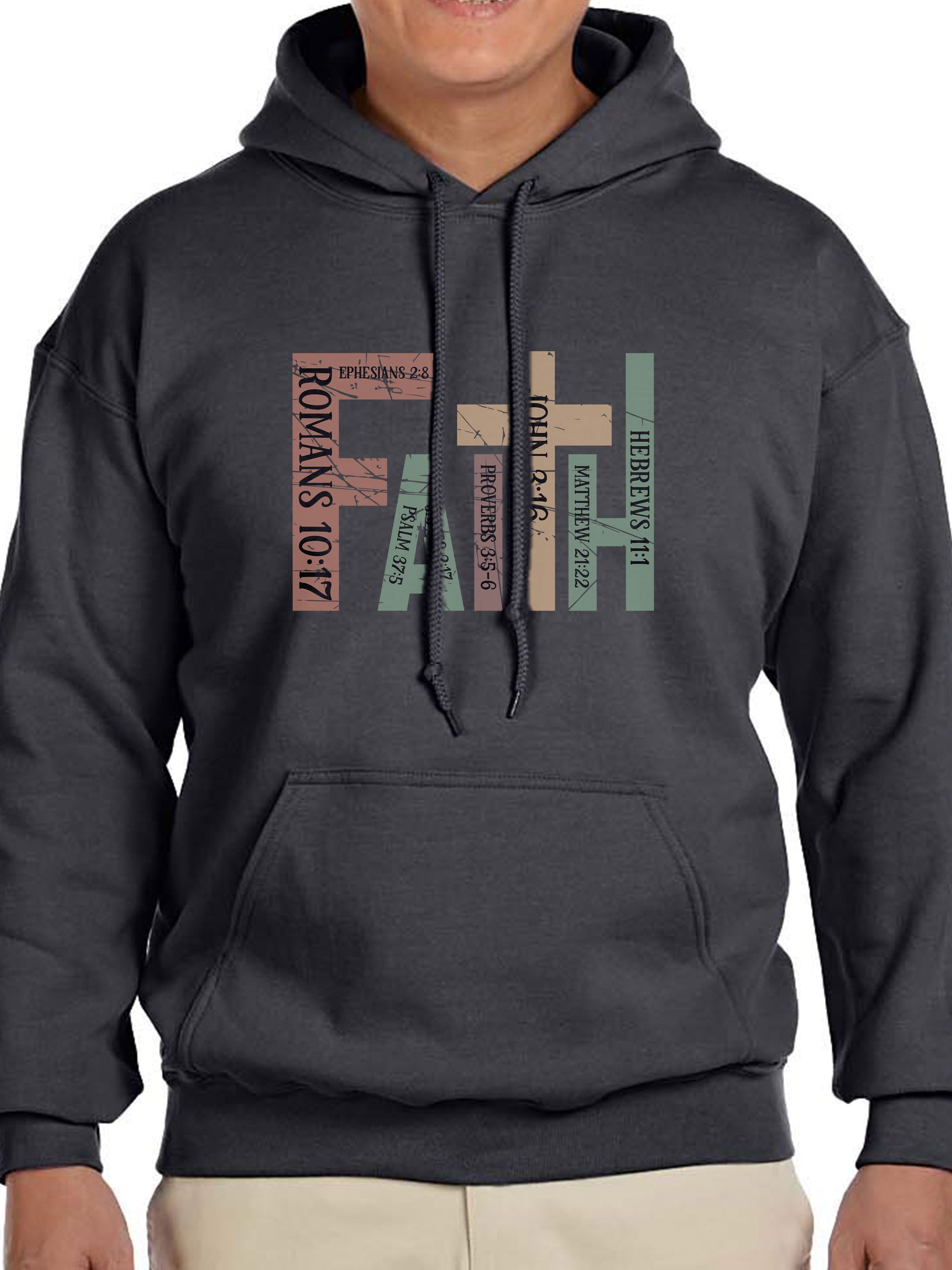 Man wearing a charcoal hoodie with the word “FAITH” printed in block letters across the chest. Each letter is filled with a Bible verse reference, including Romans 10:17, Ephesians 2:8, Psalm 37:5, Proverbs 3:5–6, John 3:16, Matthew 21:22, and Hebrews 11:1. The design combines bold typography and scripture for a powerful, faith-centered statement.