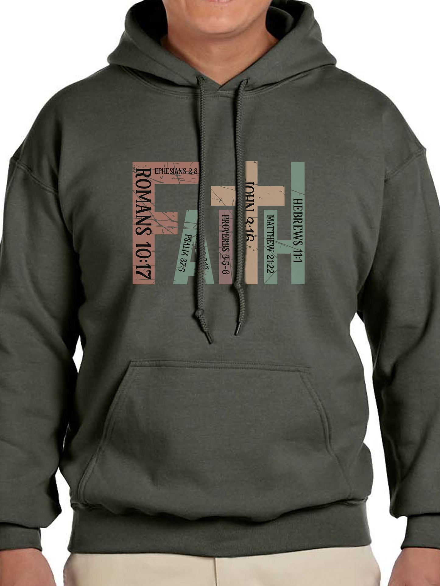 Man wearing a military green hoodie with the word “FAITH” printed in block letters across the chest. Each letter is filled with a Bible verse reference, including Romans 10:17, Ephesians 2:8, Psalm 37:5, Proverbs 3:5–6, John 3:16, Matthew 21:22, and Hebrews 11:1. The design combines bold typography and scripture for a powerful, faith-centered statement.