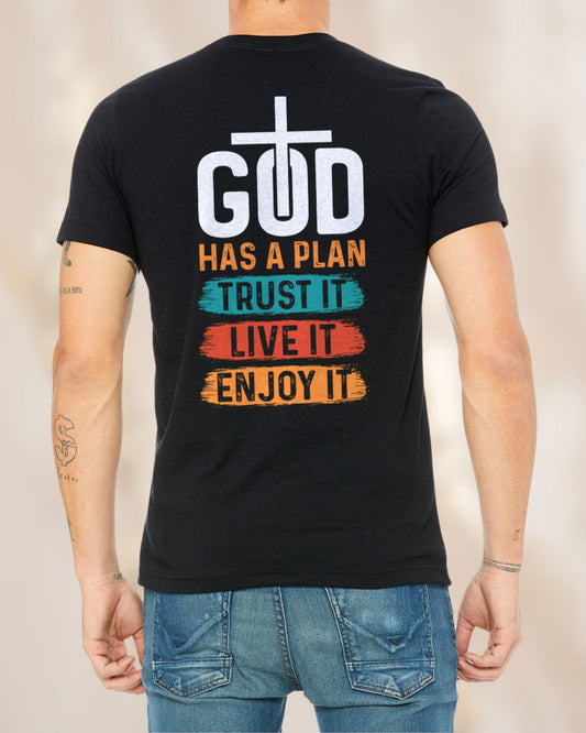 Back view of a black t-shirt with colorful brushstroke-style design reading “God Has a Plan – Trust It, Live It, Enjoy It” and a cross inside the letter “O” in “God.”