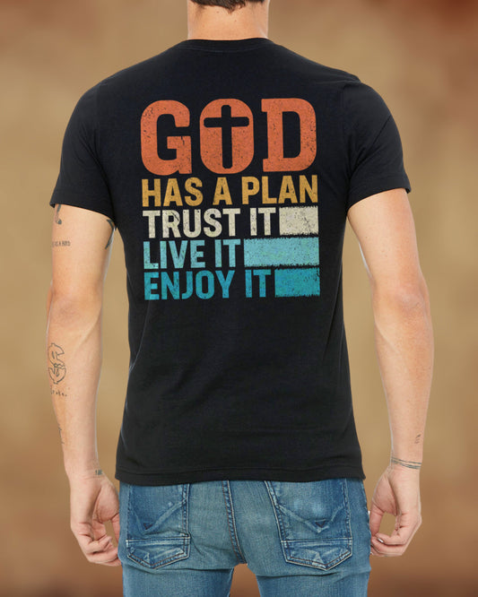 Back view of a black Christian t-shirt with bold lettering that reads “God Has a Plan – Trust It, Live It, Enjoy It” in a distressed, vintage style.