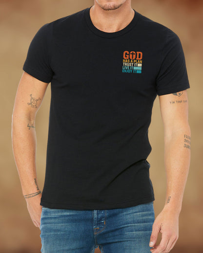 Front view of a black Christian t-shirt with bold lettering that reads “God Has a Plan – Trust It, Live It, Enjoy It” in a distressed, vintage style.
