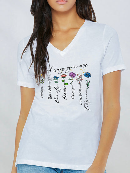 Woman wearing a white V-neck T-shirt with the phrase “God says you are” above a row of colorful flowers. Each flower is paired with a word of affirmation, including “Unique,” “Special,” “Lovely,” “Precious,” “Strong,” “Chosen,” and “Forgiven.” The design combines a gentle floral theme with faith-filled encouragement.