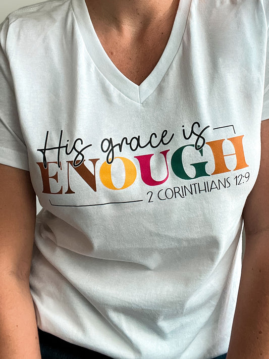 Close-up of a white V-neck T-shirt featuring the phrase “His grace is ENOUGH – 2 Corinthians 12:9.” The design highlights the word “ENOUGH” in bold, multicolored letters, emphasizing a powerful message of God’s sufficiency.