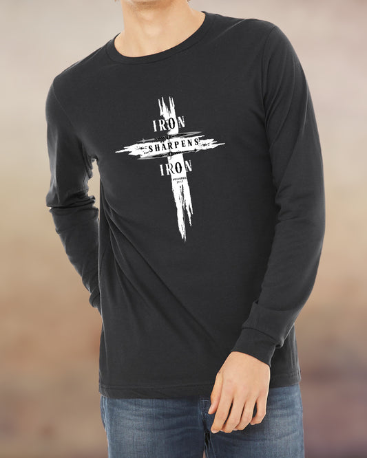 Man wearing a dark grey long-sleeve shirt with a bold white cross design that reads “Iron Sharpens Iron” from Proverbs 27:17. The graphic features a distressed brushstroke effect, giving it a rugged and powerful look suitable for faith-filled men who lead and uplift others.