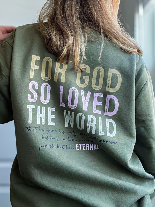 Back of a military green sweatshirt featuring the text “For God so loved the world” in large, distressed letters, followed by the full Bible verse from John 3:16 in smaller cursive script, with the word “ETERNAL” emphasized in bold. The design blends bold faith and casual comfort.