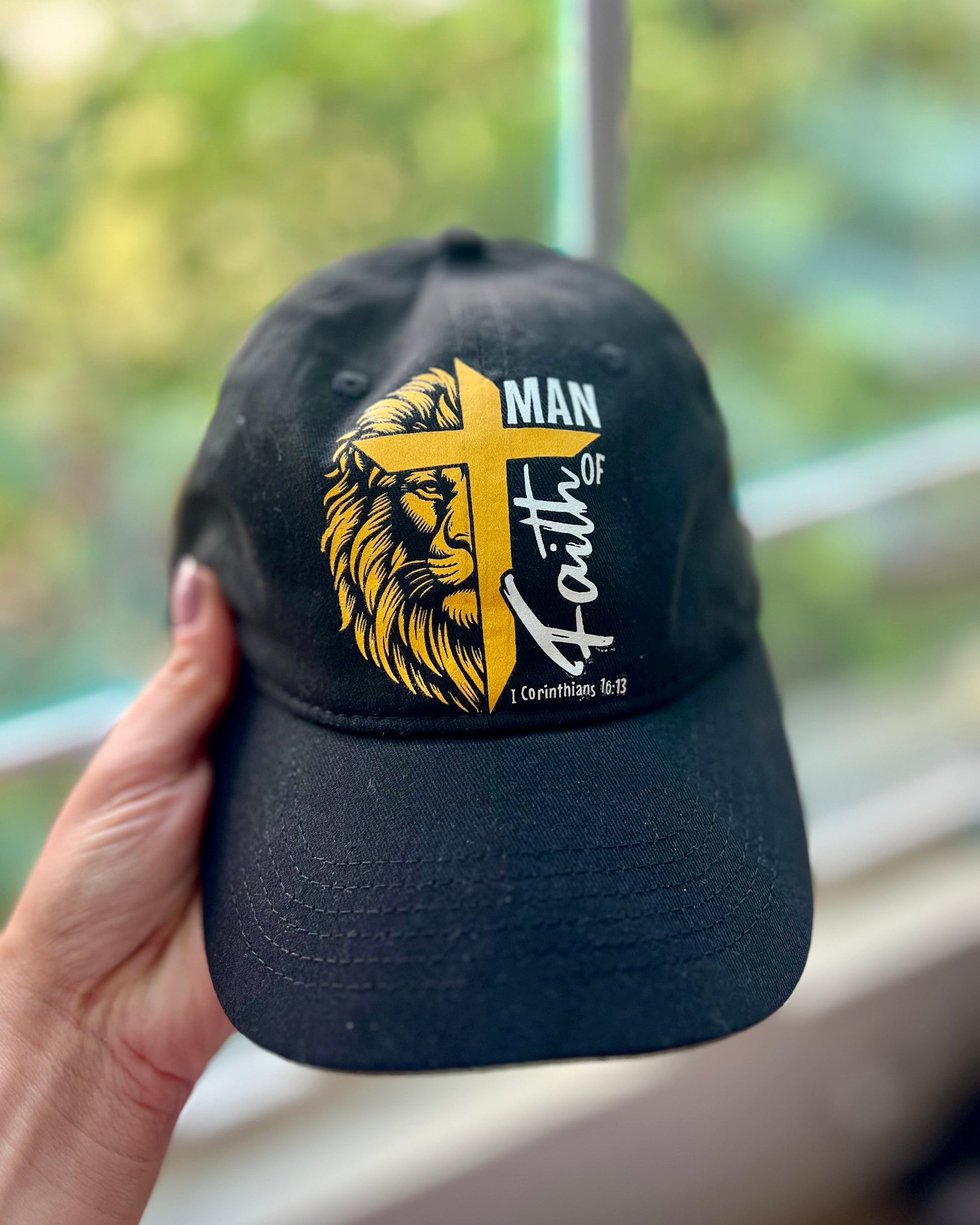Black “Man of Faith” hat with a lion and cross graphic featuring 1 Corinthians 16:13.