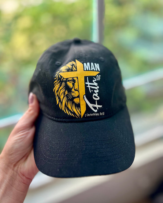 Black “Man of Faith” hat with a lion and cross graphic featuring 1 Corinthians 16:13.