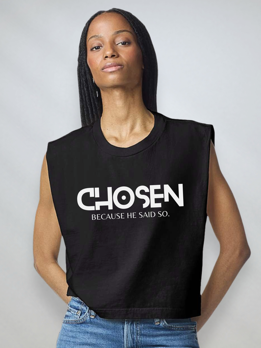 A woman wearing a black sleeveless crop top with the text 'CHOSEN BECAUSE HE SAID SO.' printed in white across the front, paired with blue jeans, against a light gray studio background.