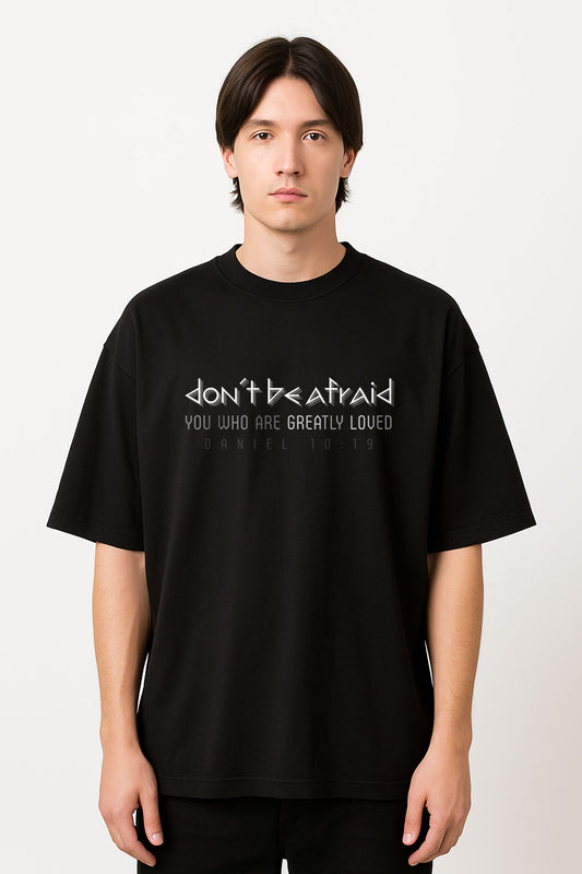 Man wearing a black oversized heavyweight Christian t-shirt featuring the Bible verse Daniel 10:19 with the message “Don’t Be Afraid”