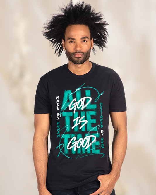 A man with a high-top afro hairstyle wearing a black graphic t-shirt with teal and white text that reads 'ALL THE TIME GOD IS GOOD' and 'MADE BY HUMAN DESIGNED BY GOD'.