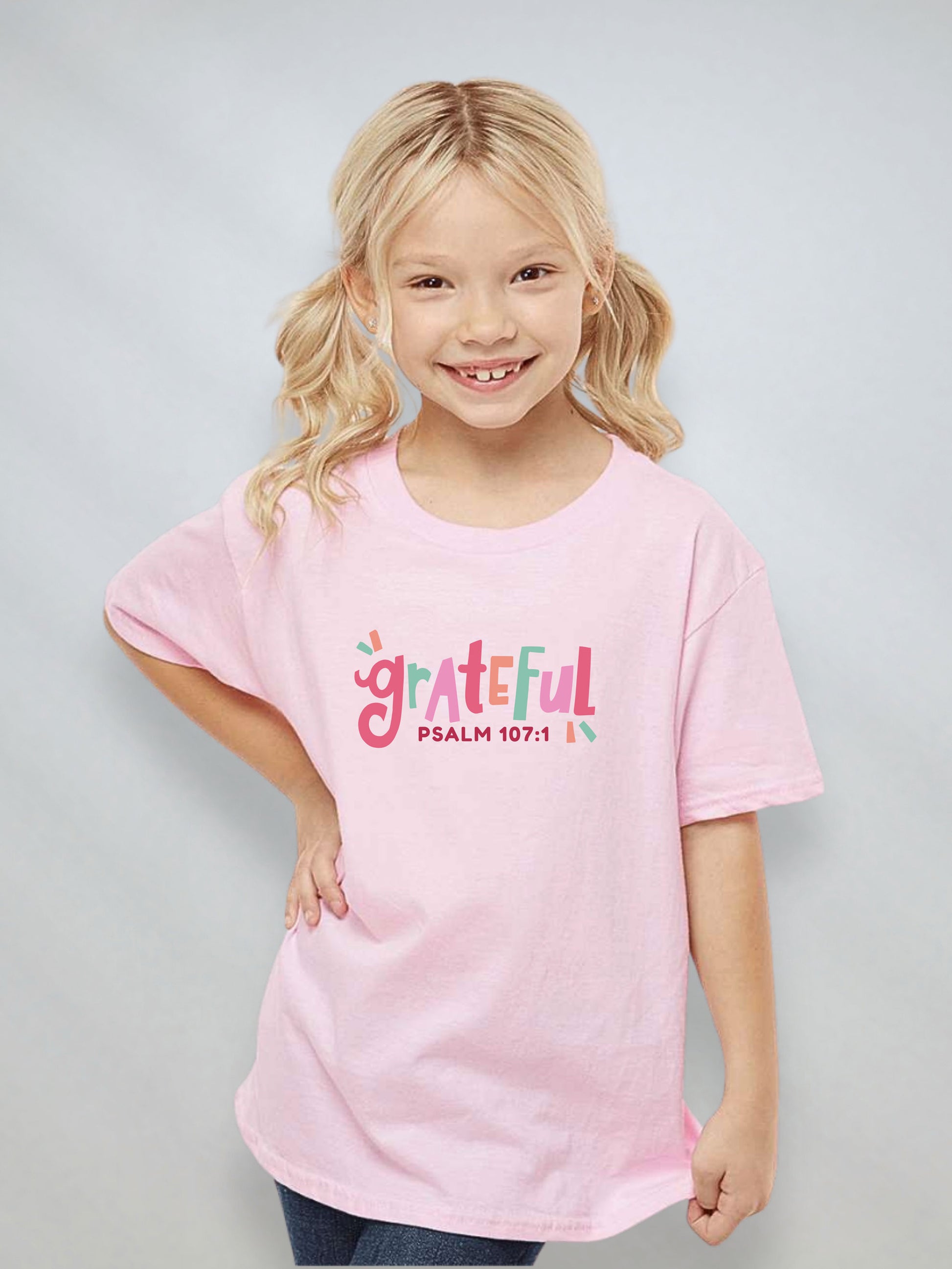 Youth girl wearing a pink Christian t-shirt with the word “Grateful” and Psalm 107:1 on the front.
