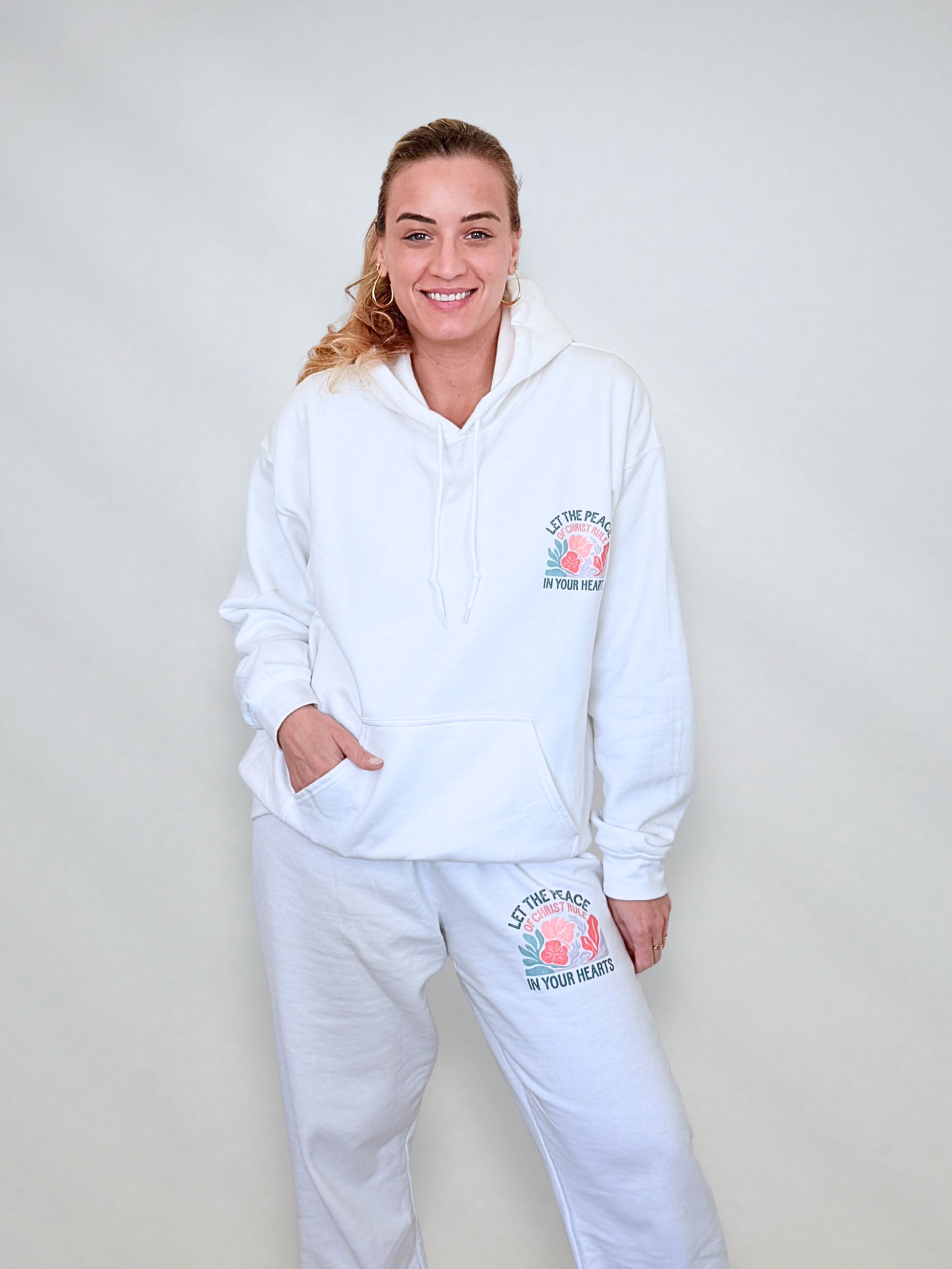 Woman wearing matching white hoodie and sweatpants set with Colossians 3:15 message.