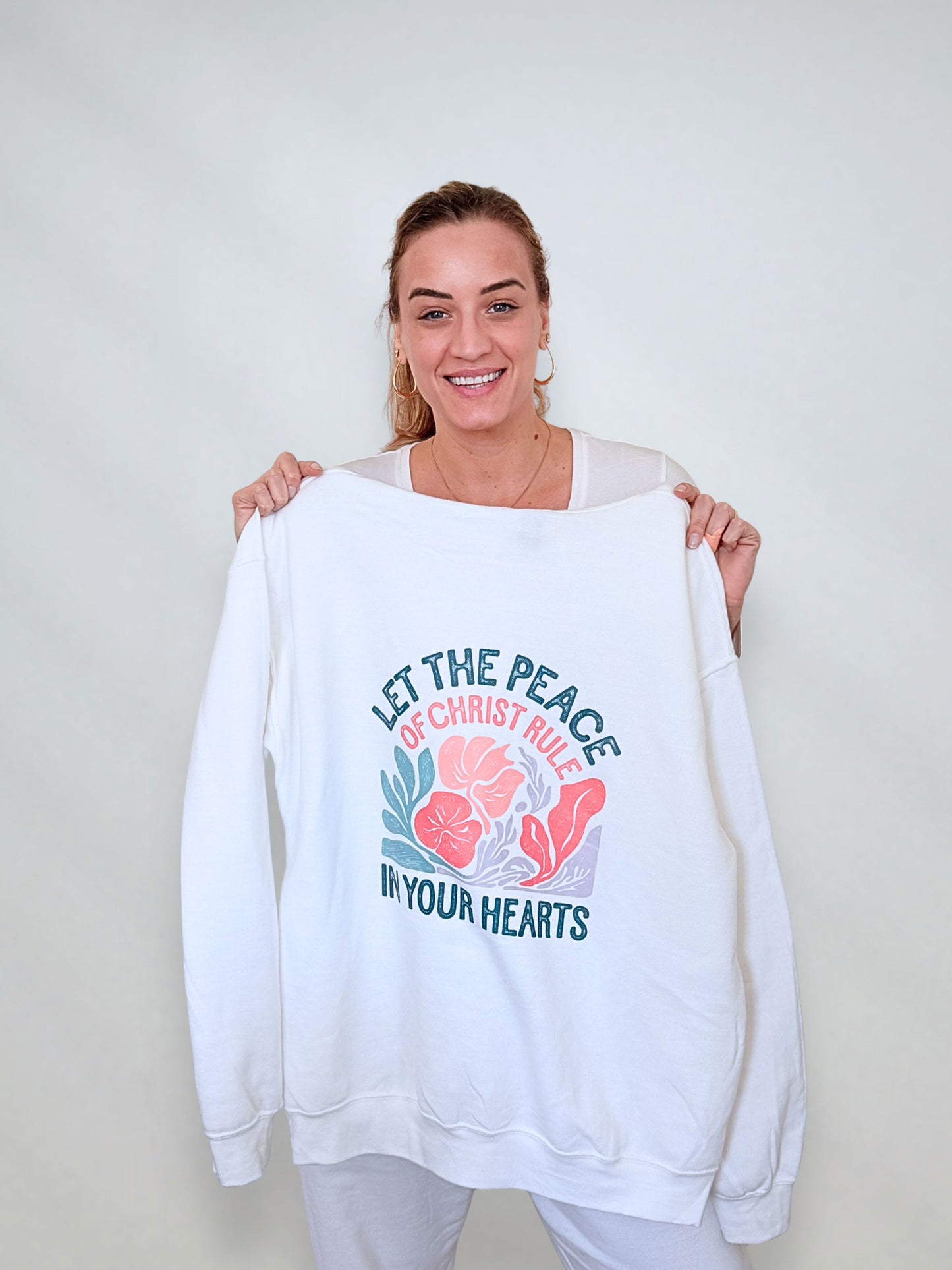 White sweatshirt with floral Christian design reading "Let the Peace of Christ Rule in Your Hearts."