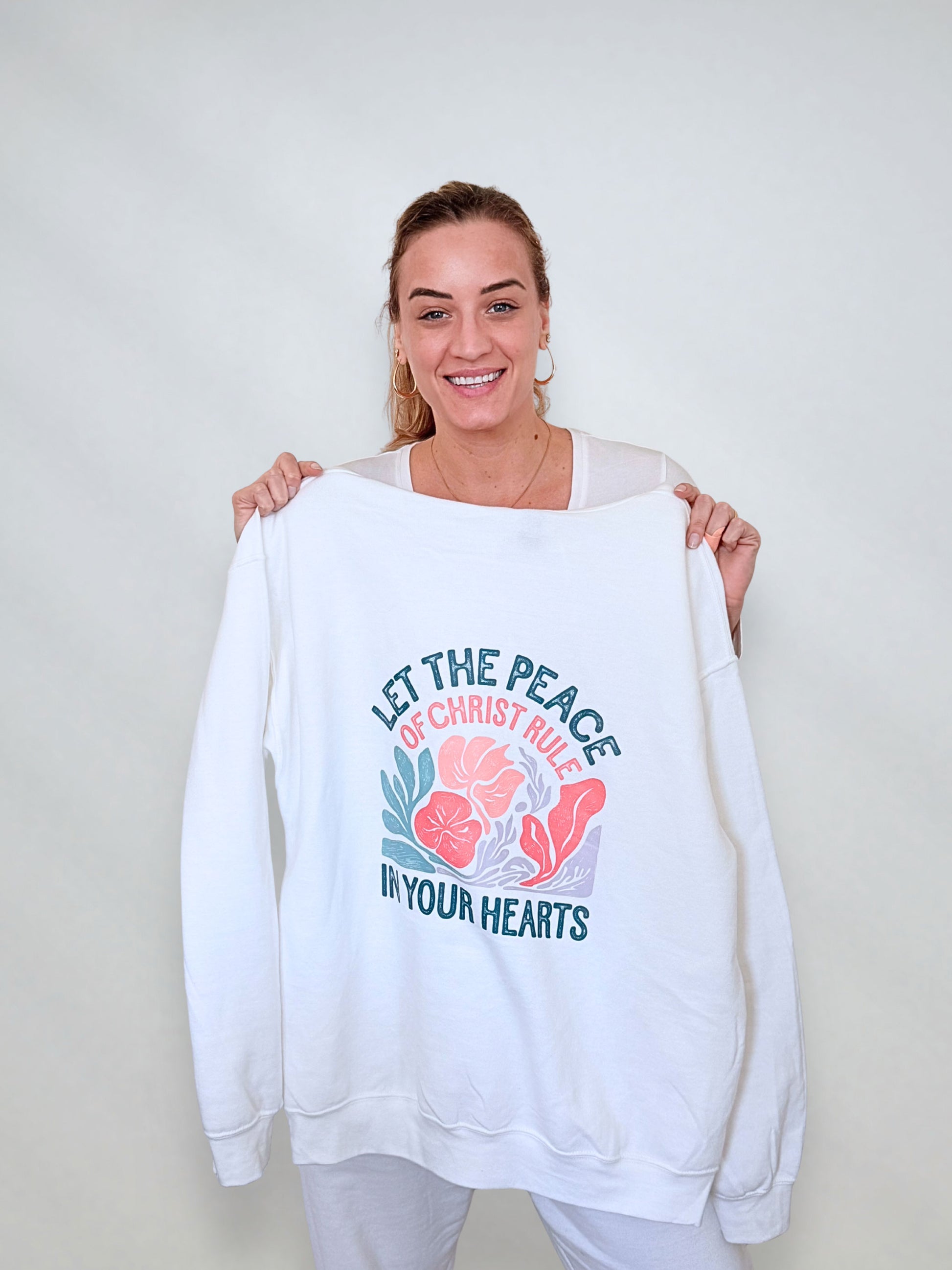 White sweatshirt with floral Christian design reading "Let the Peace of Christ Rule in Your Hearts."