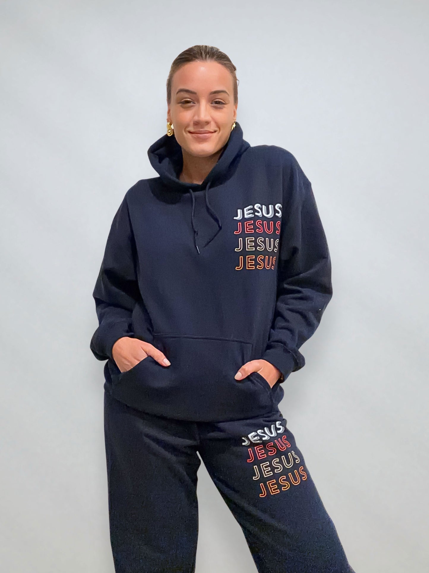 Close view of navy JESUS Repeat hoodie and sweatpants set showing stacked JESUS print on chest and leg.