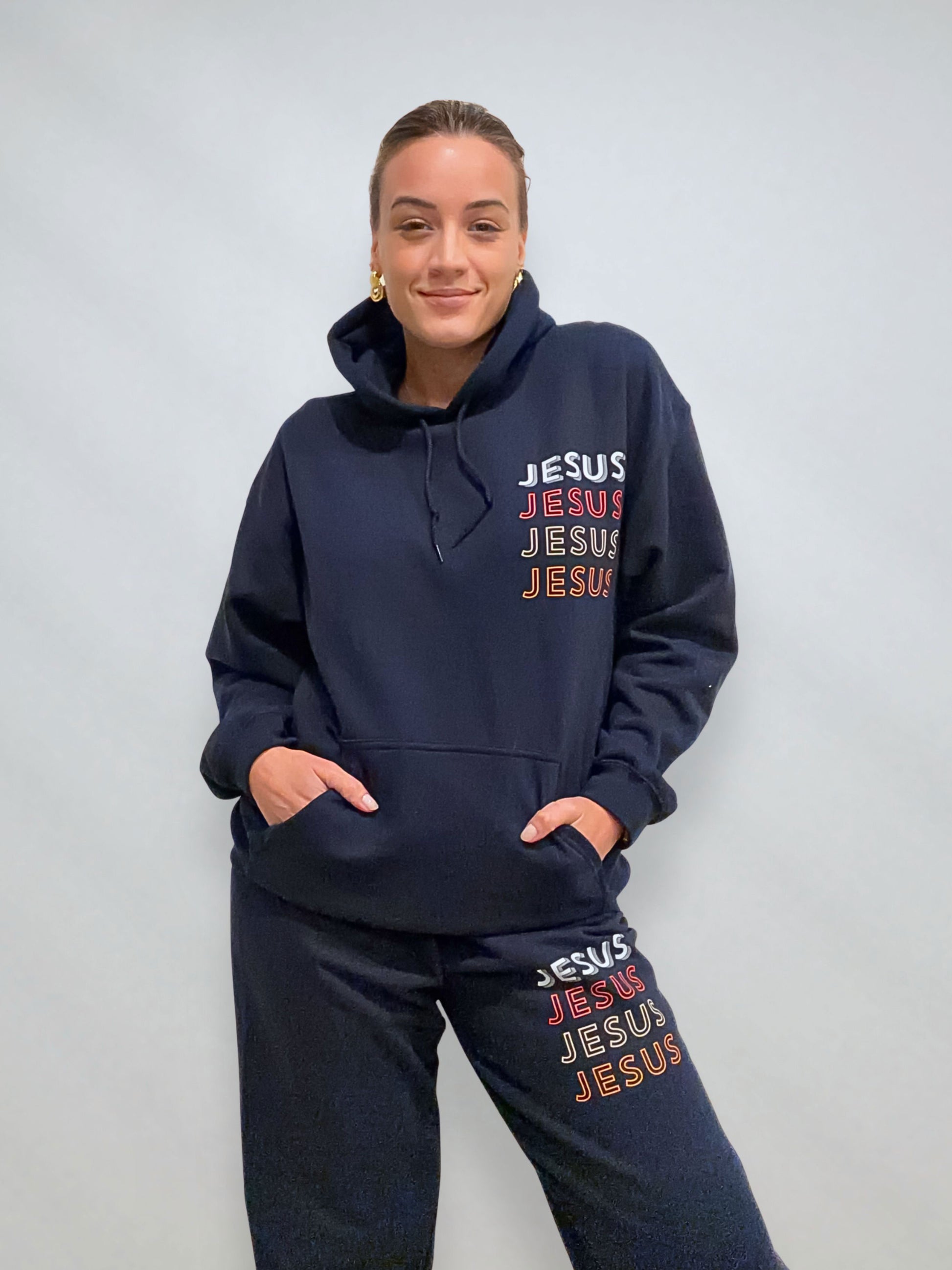 Close view of navy JESUS Repeat hoodie and sweatpants set showing stacked JESUS print on chest and leg.
