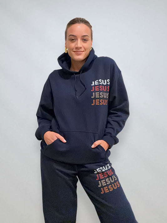 Close view of navy JESUS Repeat hoodie and sweatpants set showing stacked JESUS print on chest and leg.